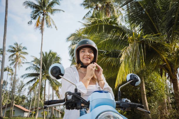 A smiling woman tights up a helmet while seated on her bike.